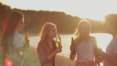 Girls-celebrate-a-birthday-on-the-open-air-party-with-friends-with-beer-and-good-mood.-They-dance-in-the-summer-evening-near-the-lake-coast.-This-is-carefree-party-at-sunset.